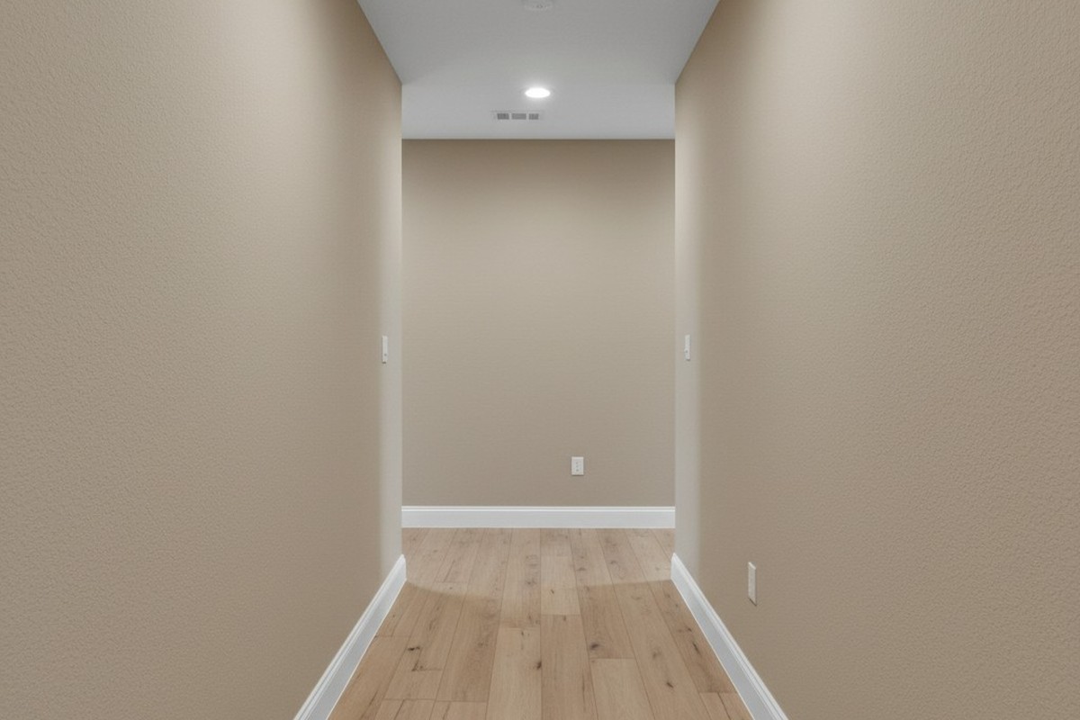 Um corredor em forma de L, bem iluminado e vazio, em uma casa moderna, com paredes bege neutro, rodapés brancos e piso laminado de carvalho claro. O espaço é uniformemente iluminado por luzes embutidas no teto.
