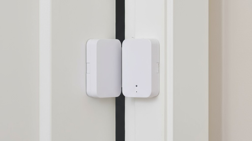 Uma foto de close-up de um sensor de contato magnético de duas partes instalado em uma porta branca e na moldura da porta.