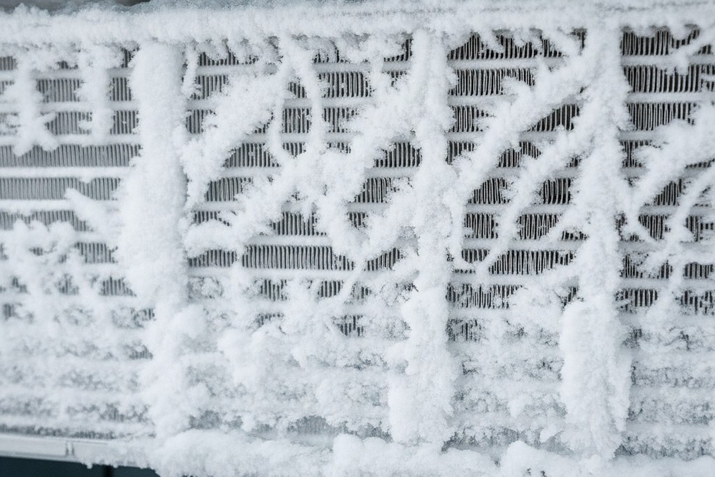 Frozen Evaporator Coil of an AC Unit A close-up of an air conditioner's evaporator coil completely encased in a thick, jagged layer of white ice and frost, obscuring the metal fins.