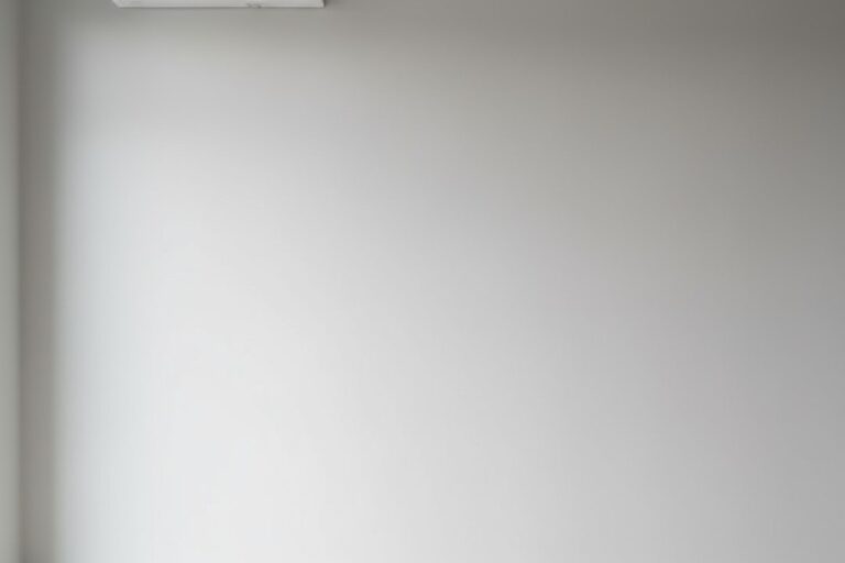 Ένα μίνιμαλ λευκό διαχωρισμένο μονάδα κλιματιστικού είναι τοποθετημένη ψηλά σε έναν ανοιχτό γκρι τοίχο σε ένα φωτεινό, σύγχρονο δωμάτιο.