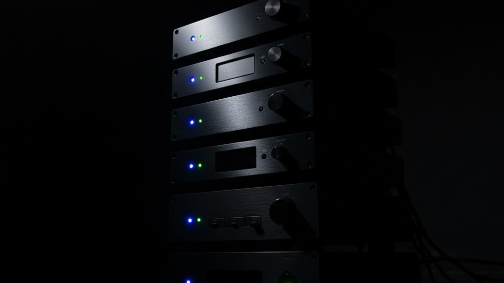 Uma pilha de equipamentos de home theater no escuro com luzes de status azuis e verdes brilhantes acesas.