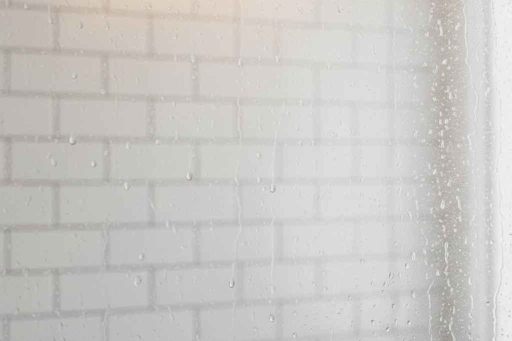 Condensação no espelho do banheiro Um espelho de banheiro fortemente embaçado com vapor, mostrando gotas de água e um reflexo borrado das paredes azulejadas.